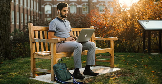 Student on bench doing work with laptop