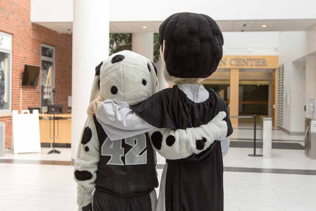 Two mascots (Huxley and Friar Dom) hugging in the Student Center