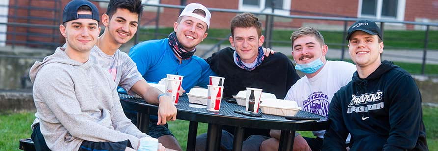 Six male students eating lunch outside at the dining hall.