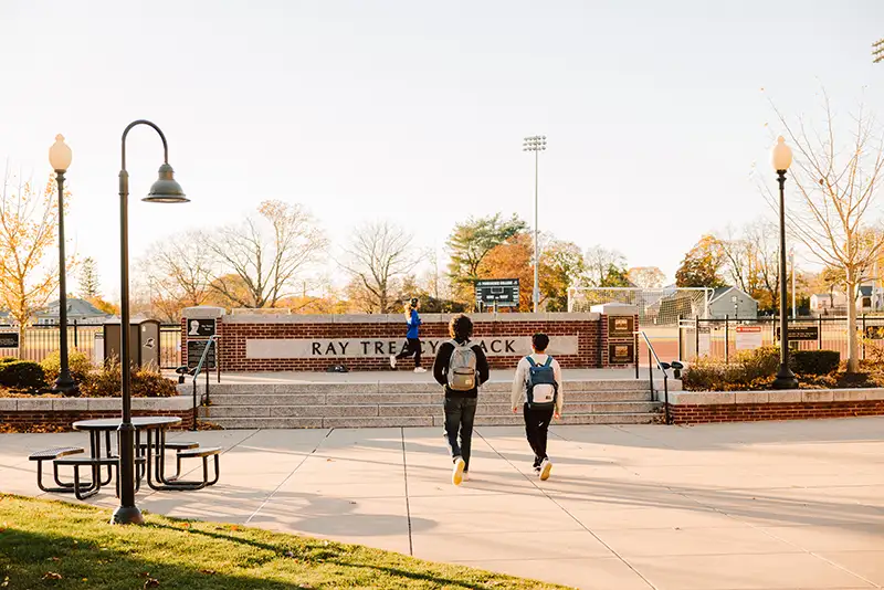 student walking on campus in the fall near the track