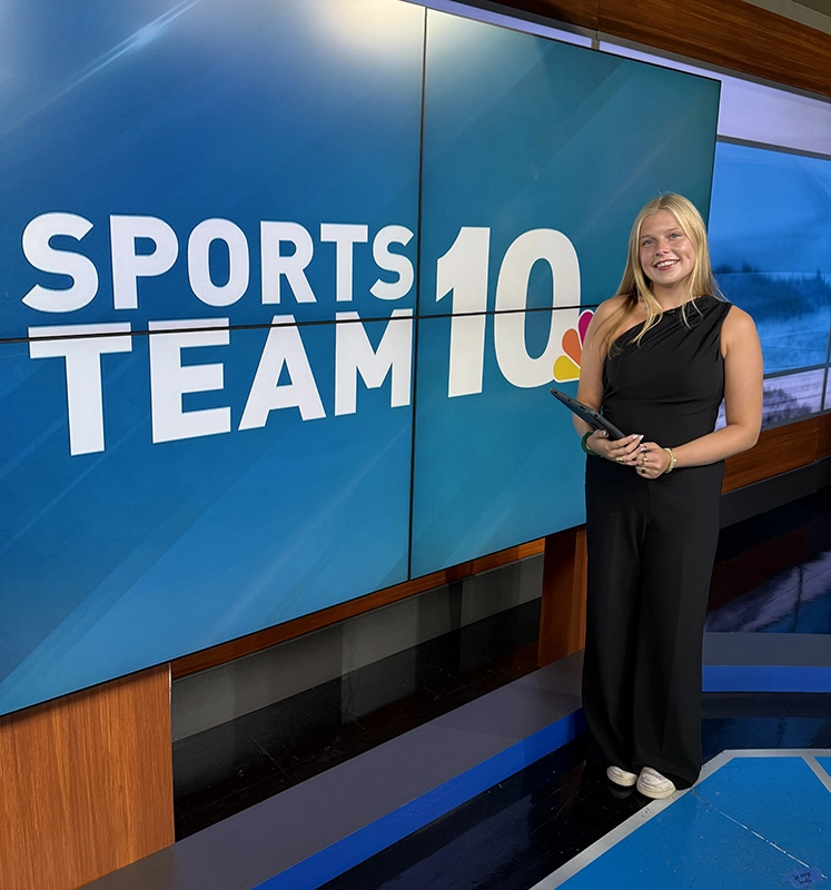 Caroline Austin '26 standing in front of the Sports Team 10 screen when interning with the NBC 10 local news station.