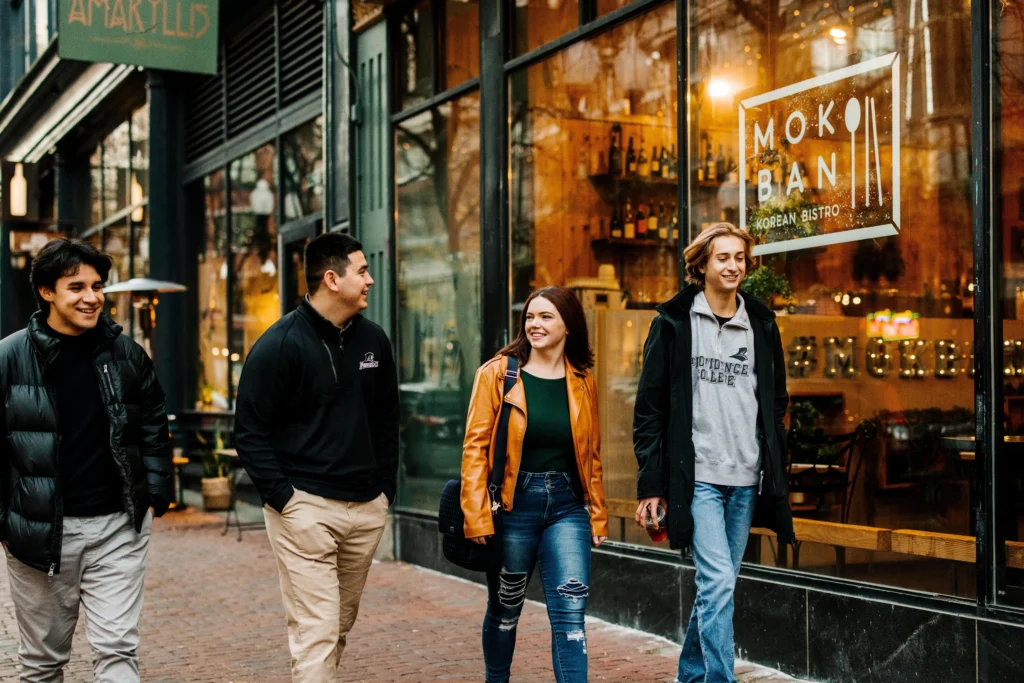 Group of four Providence College students walking past restaurants in downtown Providence