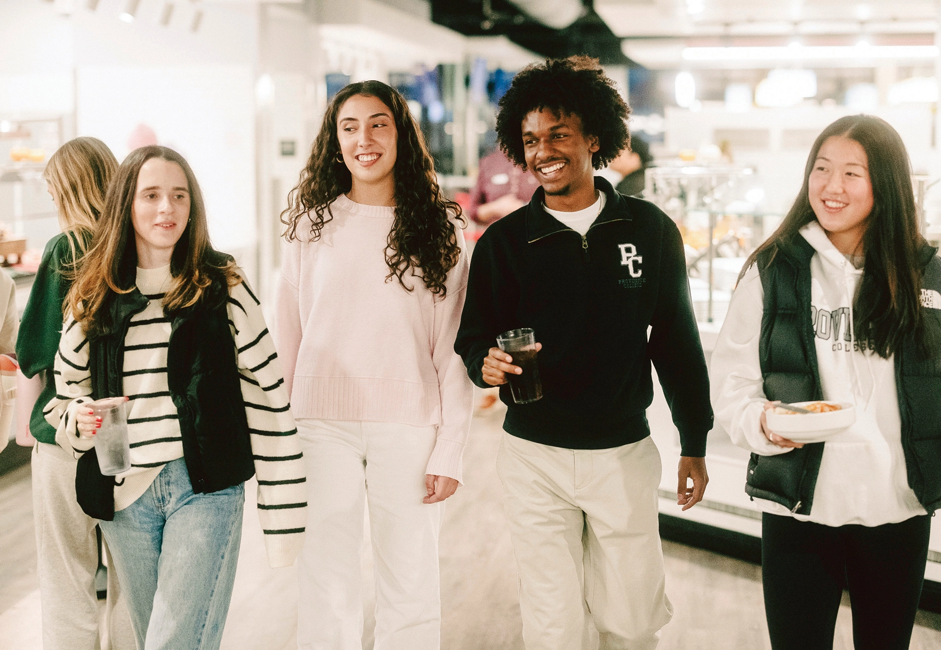 Group of four students holding food and drinks while walking in Ray