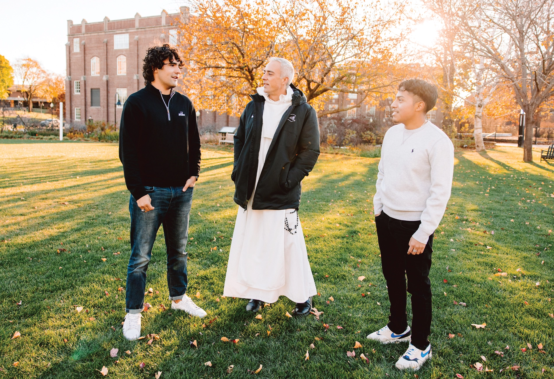 Two PC students talking with Rev. Dominic Verner, O.P. on the Slavin Lawn