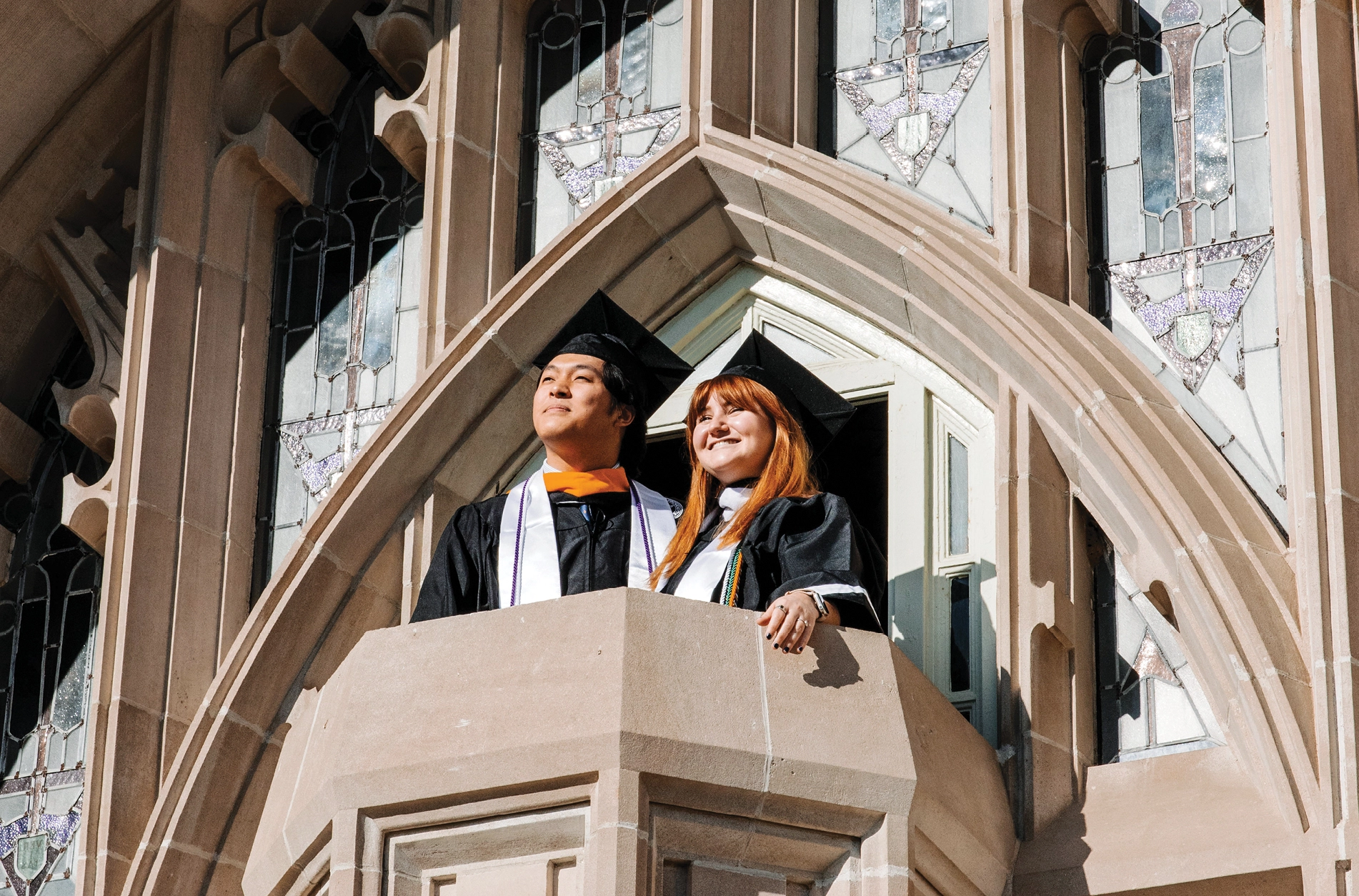 Two students standing on the balcony of Harkins Hall in their graduation attire