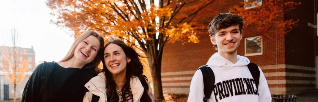 Group of three PC students laughing together while walking on campus during the fall season