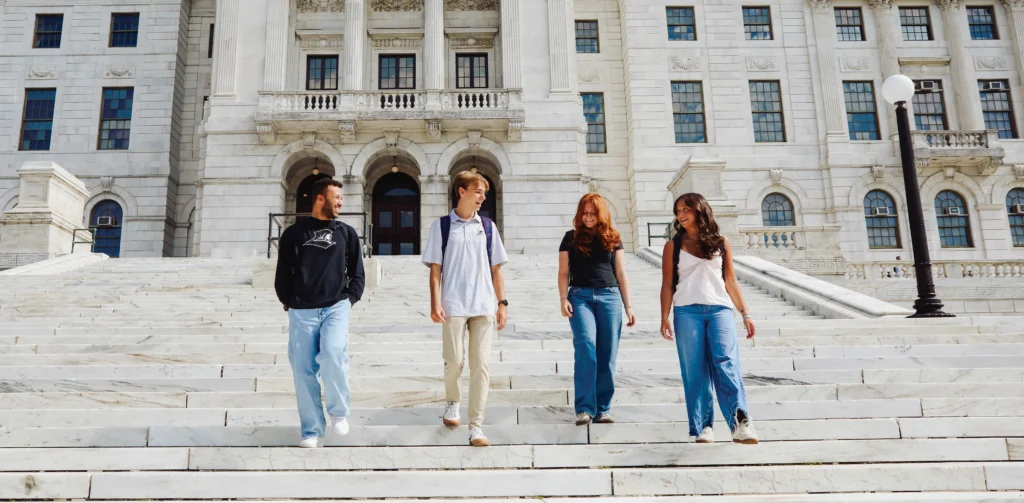Group of four PC alumni walking together down the steps of the State House in Providence